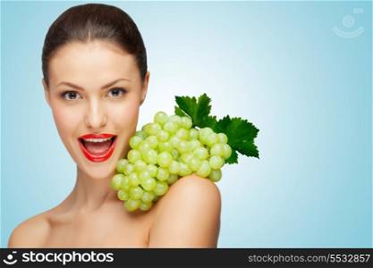 A pretty sexy woman holding a bunch of healthy green grapes on her naked shoulder.