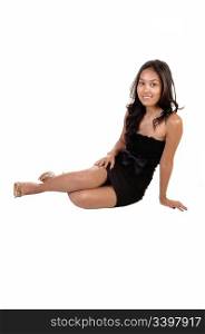 A pretty, slim Asian woman in a black dress with long curly brunette hairsitting on the floor and smiling into the camera, for white background.