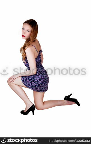 A pretty teenage girl in a blue dress with long brunette hair kneeling on the floor, isolated for white background.