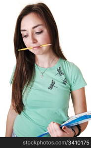 A pretty teenager in a green T-shirt and a pencil in her mouth, with long brunette hair, standing in the studio for white background.