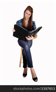 A pretty teenager sitting on a chair, in jeans and a blue chickened blousewith a notebook in her hand, for white background.