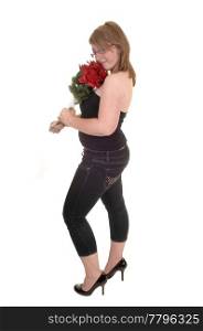 A pretty teenager standing in profile for white background, holding abunch of red roses in her hand, in jeans and high heels.