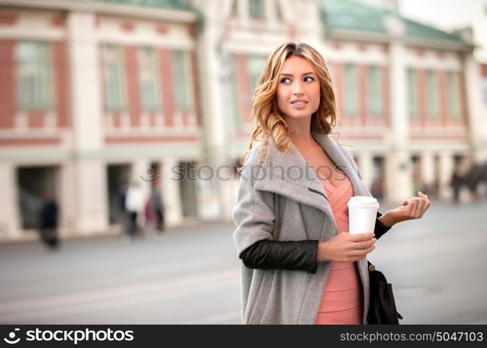 A pretty woman holding a coffee to go cup against urban scene.