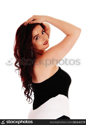 A pretty woman in a black and white dress standing in profile isolatedfor white background with her hands on her head.