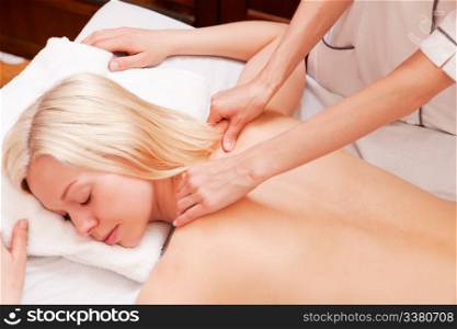 A pretty woman receiving a shoulder massage at a spa - shallow depth of field, focus on massage hands