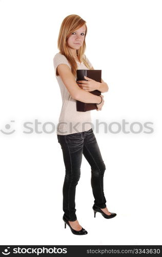 A pretty woman, standing in the studio and holding a big bookon her chest, in gray jeans and beige sweater, for white background.