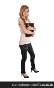 A pretty woman, standing in the studio and holding a big bookon her chest, in gray jeans and beige sweater, for white background.