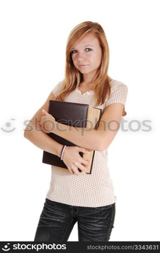 A pretty woman, standing in the studio and holding a big bookon her chest, in gray jeans and beige sweater, for white background.