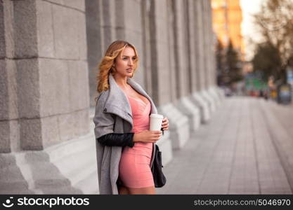 A pretty woman with a coffee to go against urban scene.