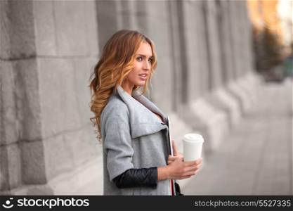 A pretty woman with a coffee to go against urban scene.