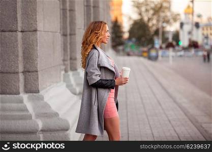 A pretty woman with a coffee to go against urban scene.