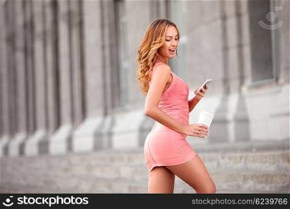 A pretty woman with a mobile phone holding a take away coffee against urban scene.
