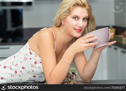 a pretty young blond woman drinking coffee in the kitchen