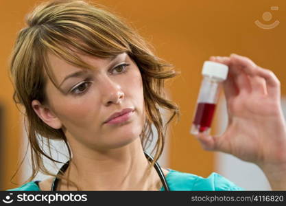 A pretty young female doctor in scrubs with a stethoscope examines a blood sample intently