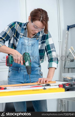 a pretty young smiling woman using cordless drill