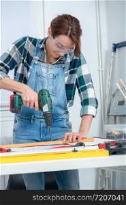 a pretty young smiling woman using cordless drill
