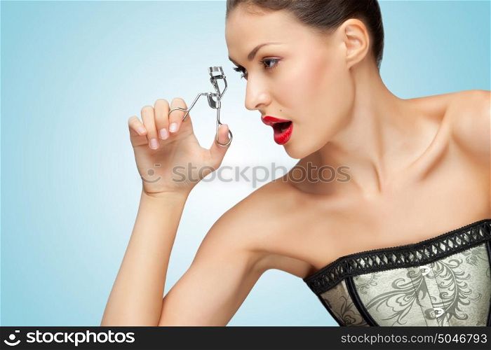 A pretty young woman holding an eyelash curler in her hand.