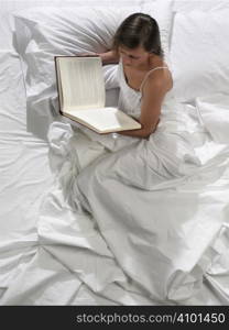 A pretty young woman reads a book in bed