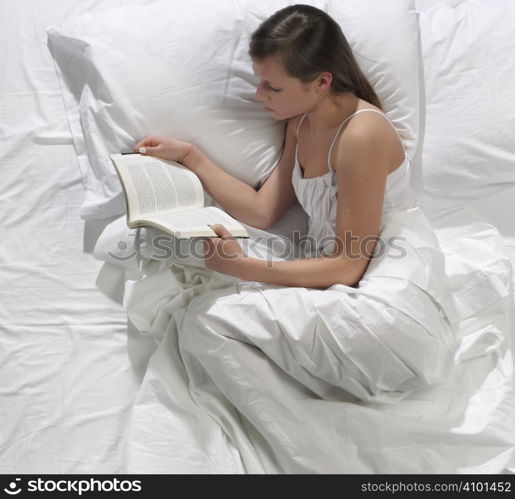 A pretty young woman reads a book in bed