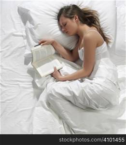 A pretty young woman reads a book in bed