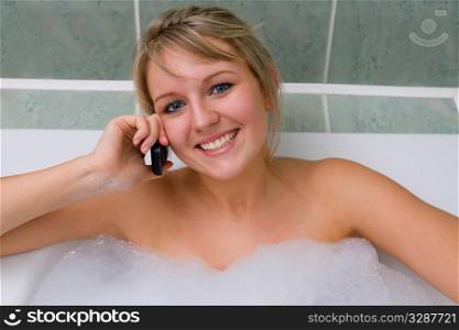 A pretty young woman relaxing in a bubble bath and chatting on her mobile phone
