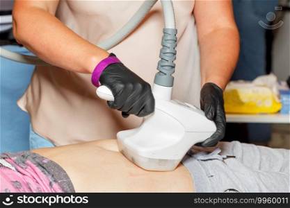 A professional beautician in latex black gloves performs an electromagnetic massage of the abdominal muscles on a vacuum simulator.. The beautician conducts a session of massage of the abdominal muscles using a vacuum electric massager.