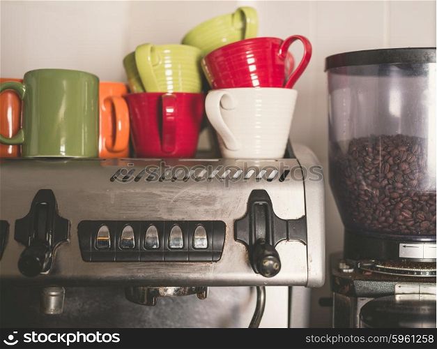 A professional coffee machine with beans in the grinder and colorful cups on top of it