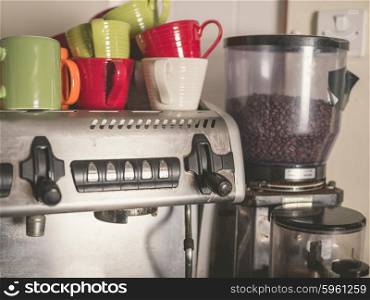 A professional coffee machine with beans in the grinder and colorful cups on top of it