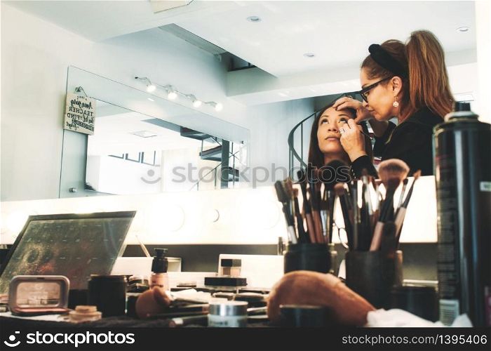 A professional makeup artist in a studio painting a woman?s face - people reflected in mirror