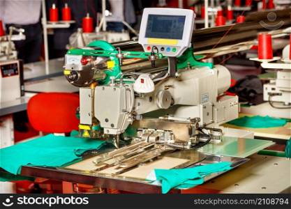A professional multitasking sewing machine with a screen for programming various functions close-up against the background of a factory sewing workshop in a blurred view.. Modern sewing equipment in a sewing factory, a sewing machine with programmable functions close-up.