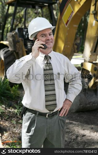 A proud, confident engineer on the construction site, talking on the telephone.