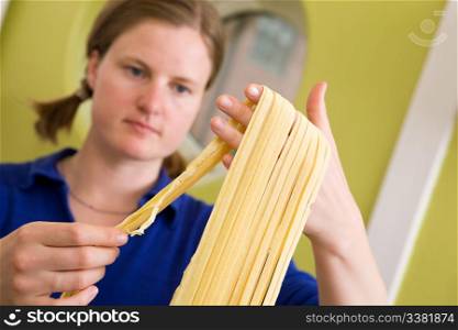 A proud young woman with fresh homemade fettuccine - shallow depth of field with focus on the pasta