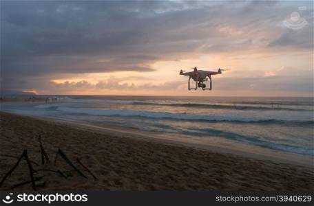 A radio controlled quad copter flys by as the sun sets