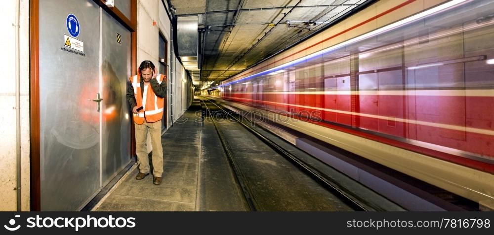 A railroad engineer, covering his ears from the thunder of a passing tram inside a tunnel, just before he reaches the door.