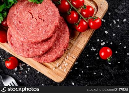 A raw burger on a tomato cutting board. On a black background. High quality photo. A raw burger on a tomato cutting board.