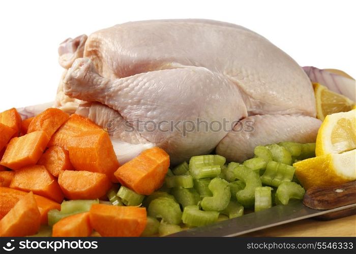 A raw chicken and the ingredients for pot-roasting it - carrots, lemon, onion and celery against a white background