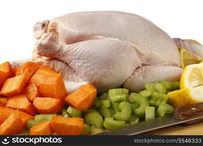 A raw chicken and the ingredients for pot-roasting it - carrots, lemon, onion and celery against a white background