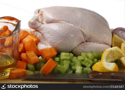A raw chicken and the ingredients for pot-roasting it - olive oil, carrots, lemon, onion and celery against a white background
