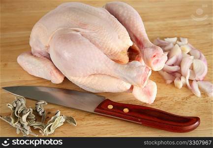 A raw chicken on a chopping board with dried sage, chopped onion and a knife