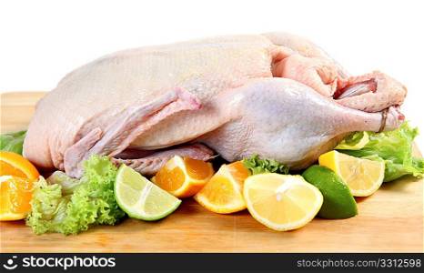 A raw duck on a chopping board, with segments of lemon, orange and lime and lettuce leaves.
