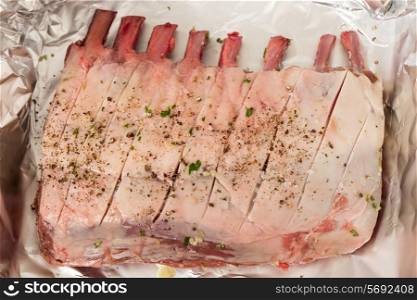 A raw rack of lamb rubbed with pepper, salt, herbs and garlic, on tinfoil before being roasted.