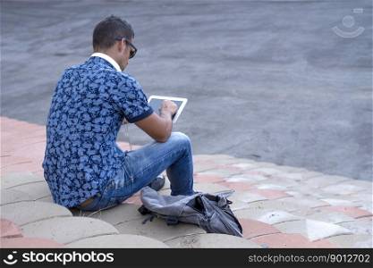 A Rear image of young man sitting on bleachers using a tablet