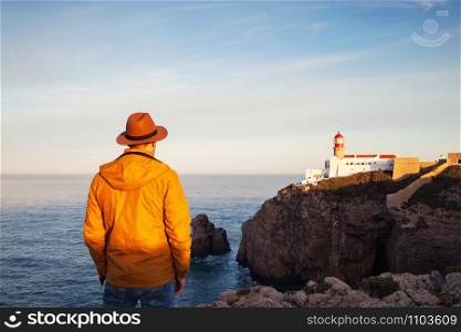 A rear view of of a lone man in hat standing on a cliff top with an inspiring ocean view on cape Vicente Lighthouse, Portugal