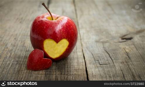 A red apple with engraved heart on wood background