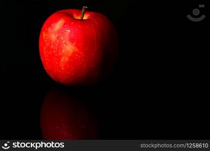 A red apple with water drops on skin isolated on black background with copy space. Healthy fruit and healthy food concept. Vegan food.
