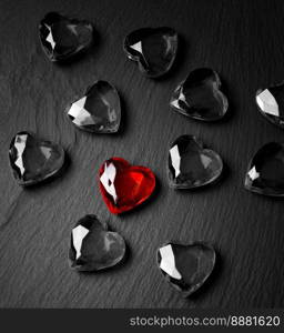 A red crystal in the shape of a heart lies on a dark background among black and white crystals.