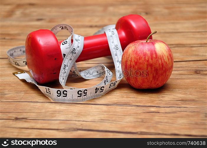 A Red dumbbell on a wooden background with a measuring tape and an apple