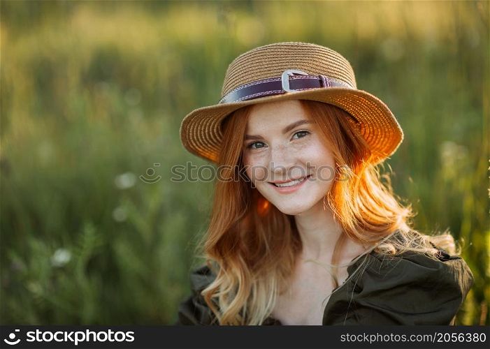 A red-haired girl among dandelions in the summer in the field.. A red-haired young girl is sitting in a meadow among dandelions 3627.