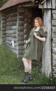 A red-haired girl in a green rustic dress rejoices in the sun.. A village pastoral with a red-haired young girl 3259.