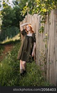 A red-haired girl in a green rustic dress rejoices in the sun.. A village pastoral with a red-haired young girl 3261.